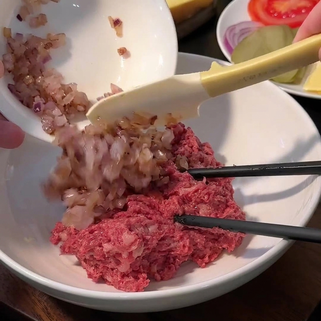 大きなボウルに入った、混ぜる前の牛ひき肉、パン粉、塩、胡椒、炒めた玉ねぎ。