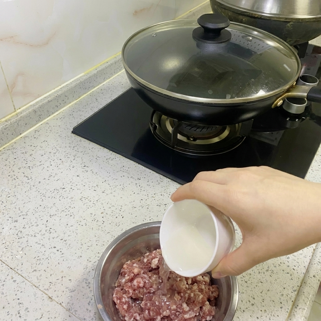 ステンレスボウルに入った生挽肉に、玉ねぎと生姜の絞り汁を注いでいる様子。