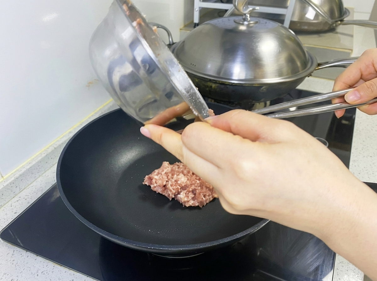 熱したフライパンで、挽肉をパティの形に整えている様子。
