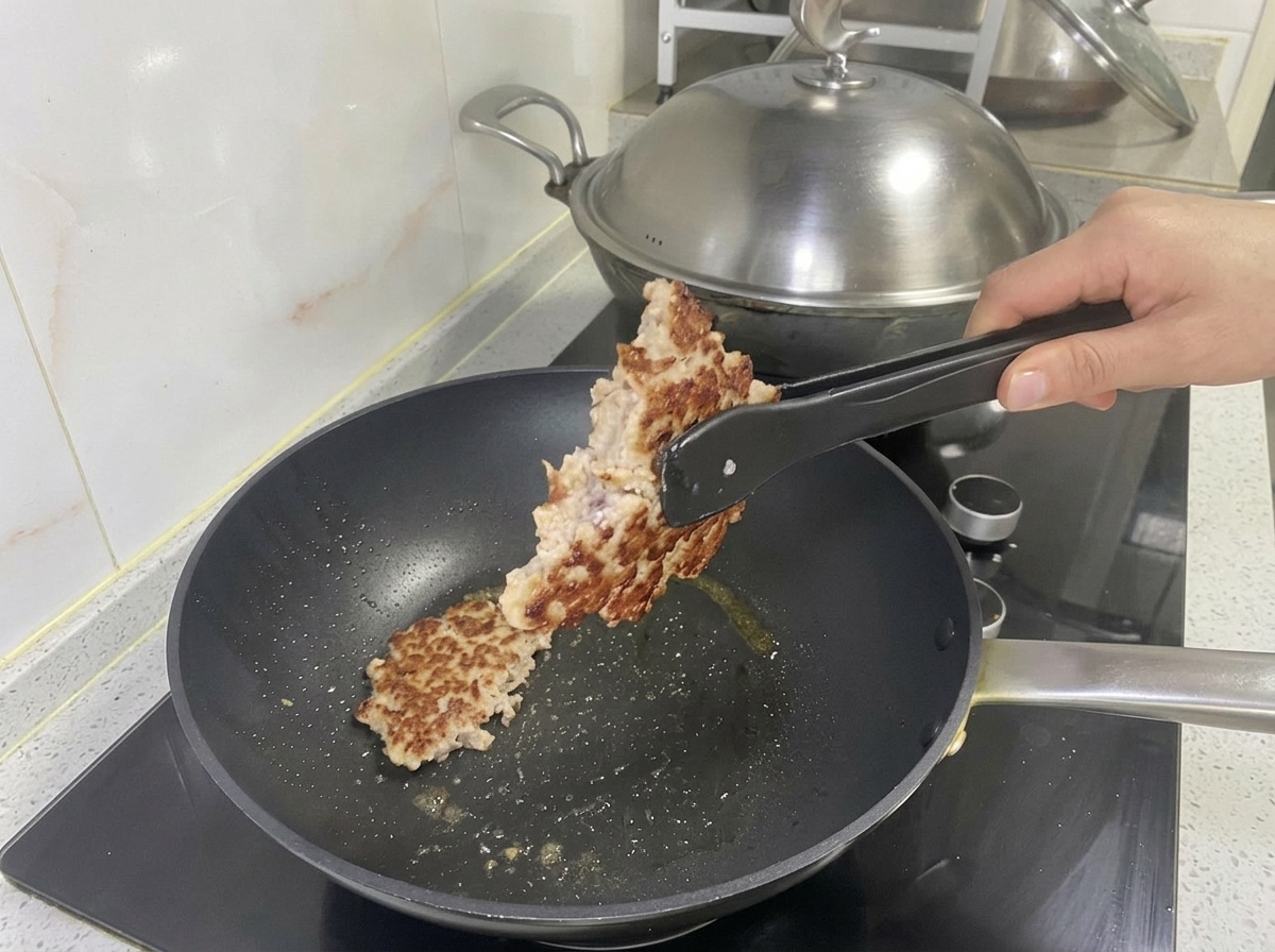 トングで焼き上がった黄金色の豚肉パティを持ち上げている様子。