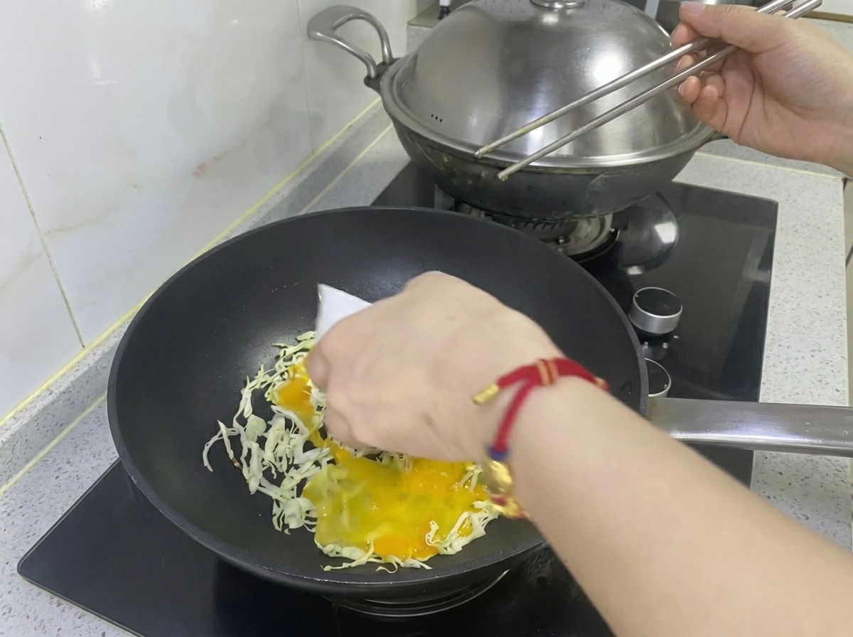 フライパンのキャベツの上に、溶き卵を回し入れている様子。