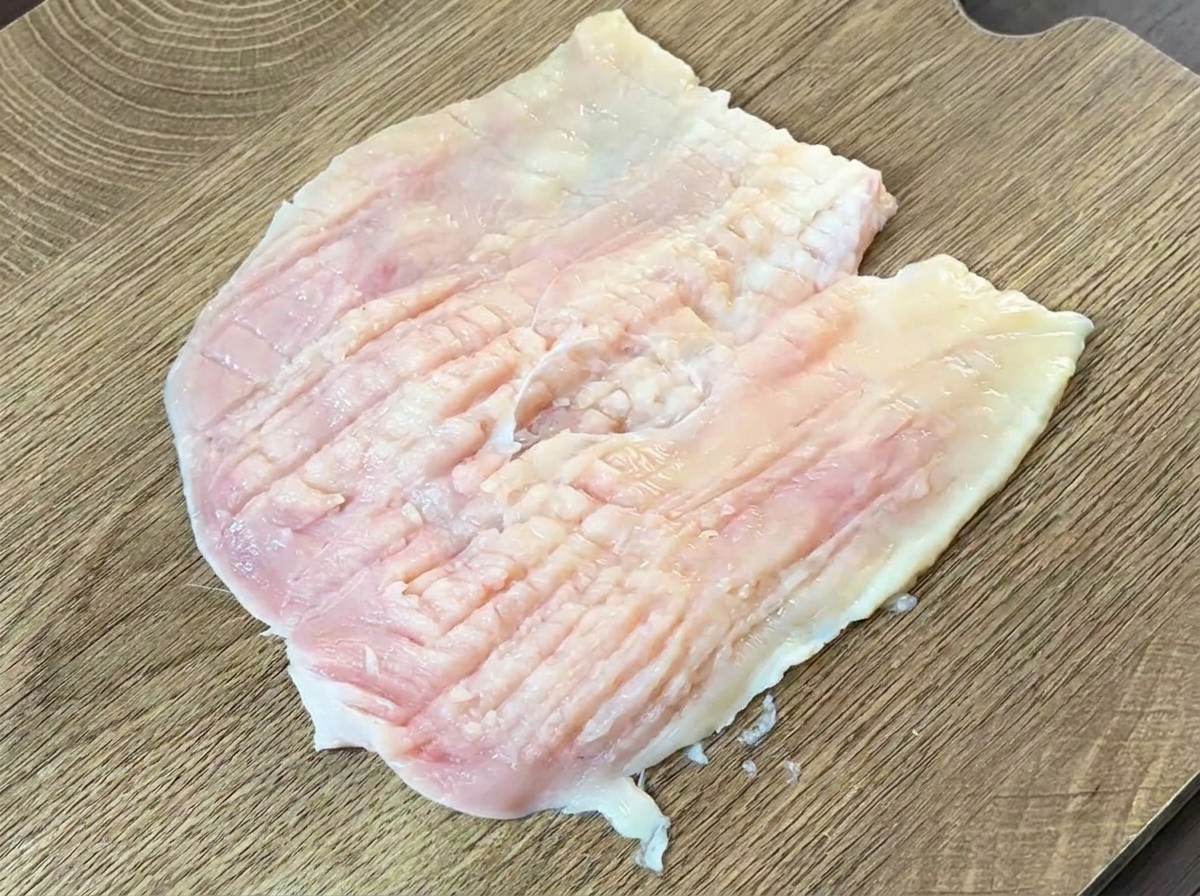 包丁の背を使って鶏むね肉を叩いて平らにしている様子。