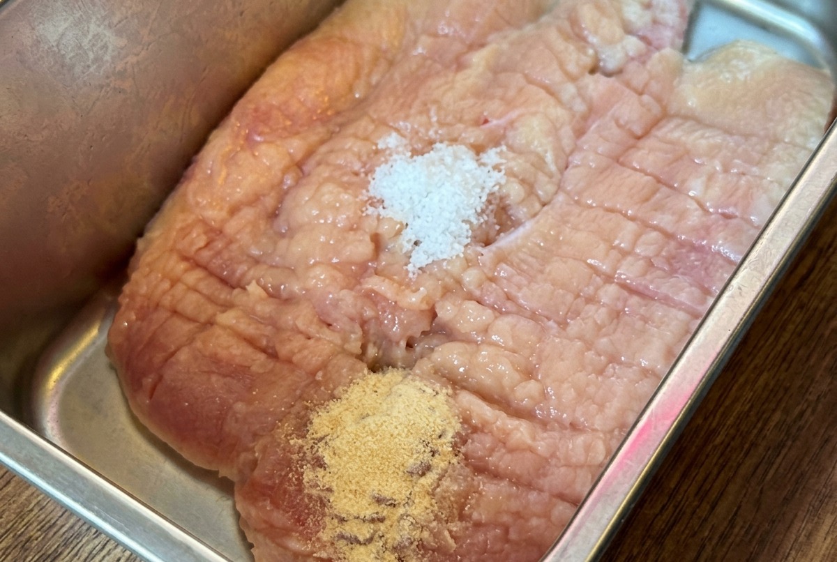 トレイにのせた鶏肉にスパイスとソースをかけている様子。