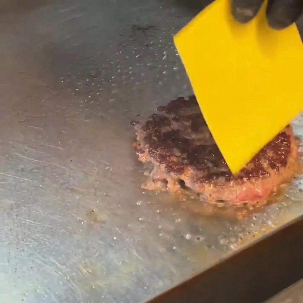 焼いたビーフパティの上で、バーナーを使ってチーズを溶かしている様子。