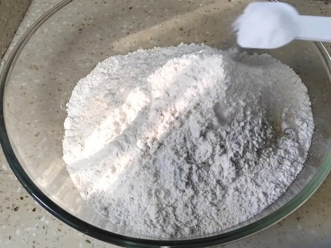 ガラスのボウルに入った小麦粉にスプーンで塩を加えている様子。