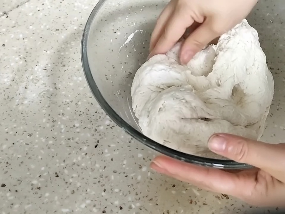 ガラスボウルの中で生地を練り合わせている手。