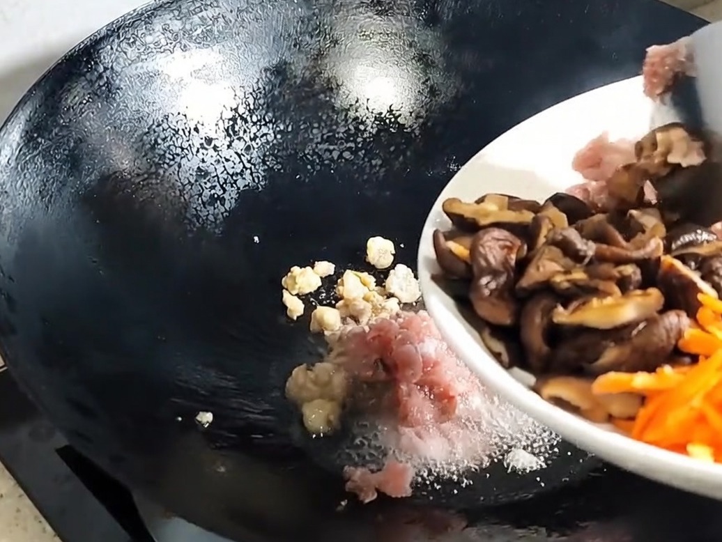 炒めた豚肉に椎茸と具材を加えて炒めている様子。