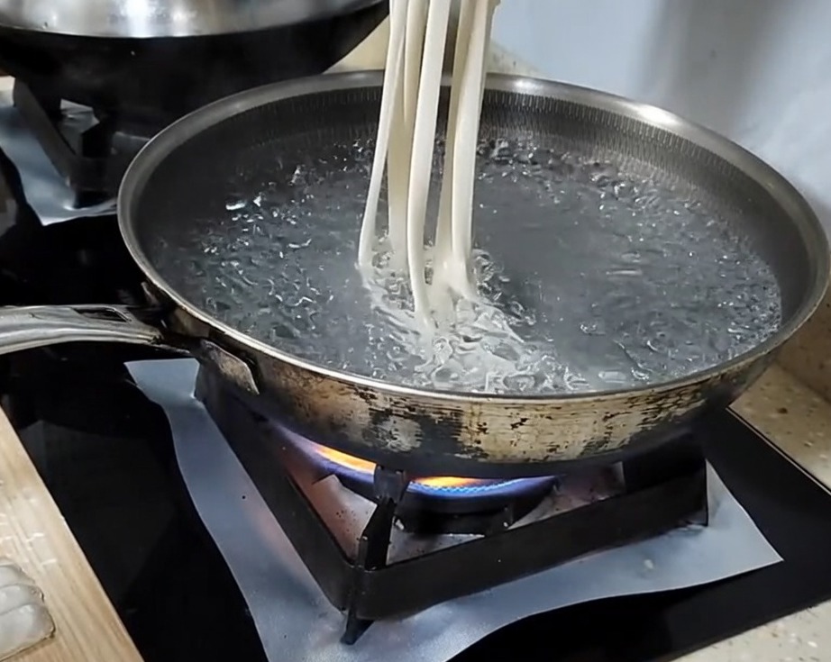 手で麺を伸ばしながら沸騰したお湯に入れている様子。