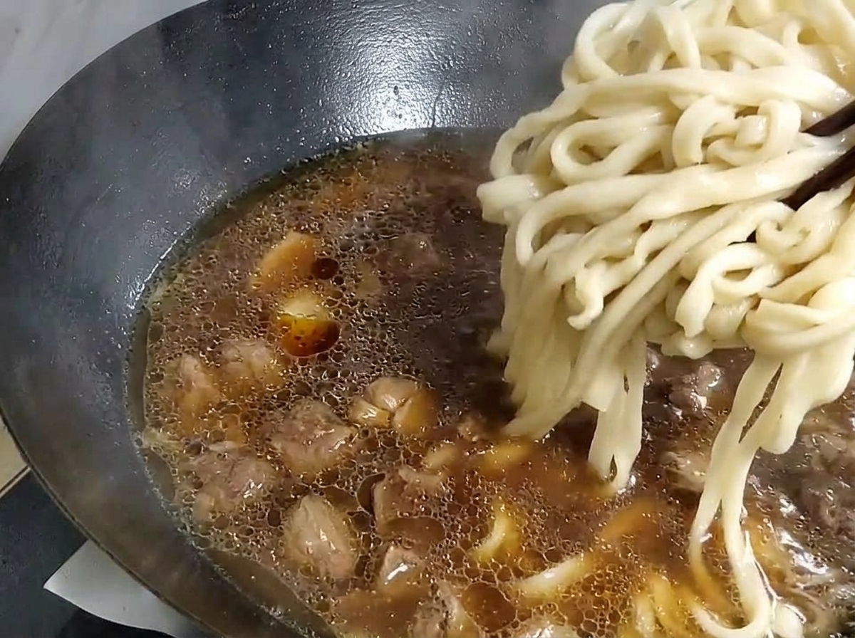 茹で上がった麺をスープの入った中華鍋に移している様子。