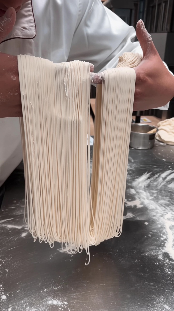 職人の手からしなやかに垂れ下がる、細く均一に伸びた手延べ麺の束。
