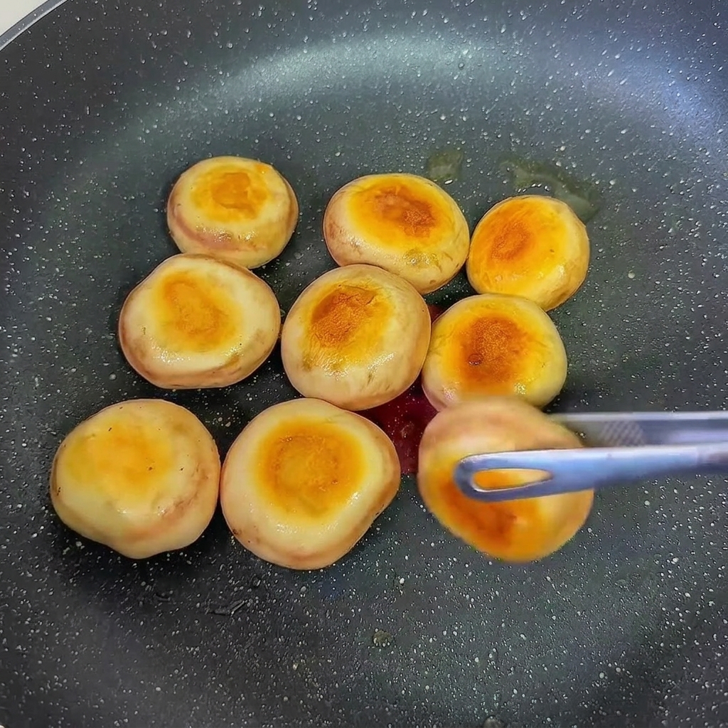 フライパンで両面を焼いて焼き色をつけている、海老のすり身を詰めたマッシュルーム。