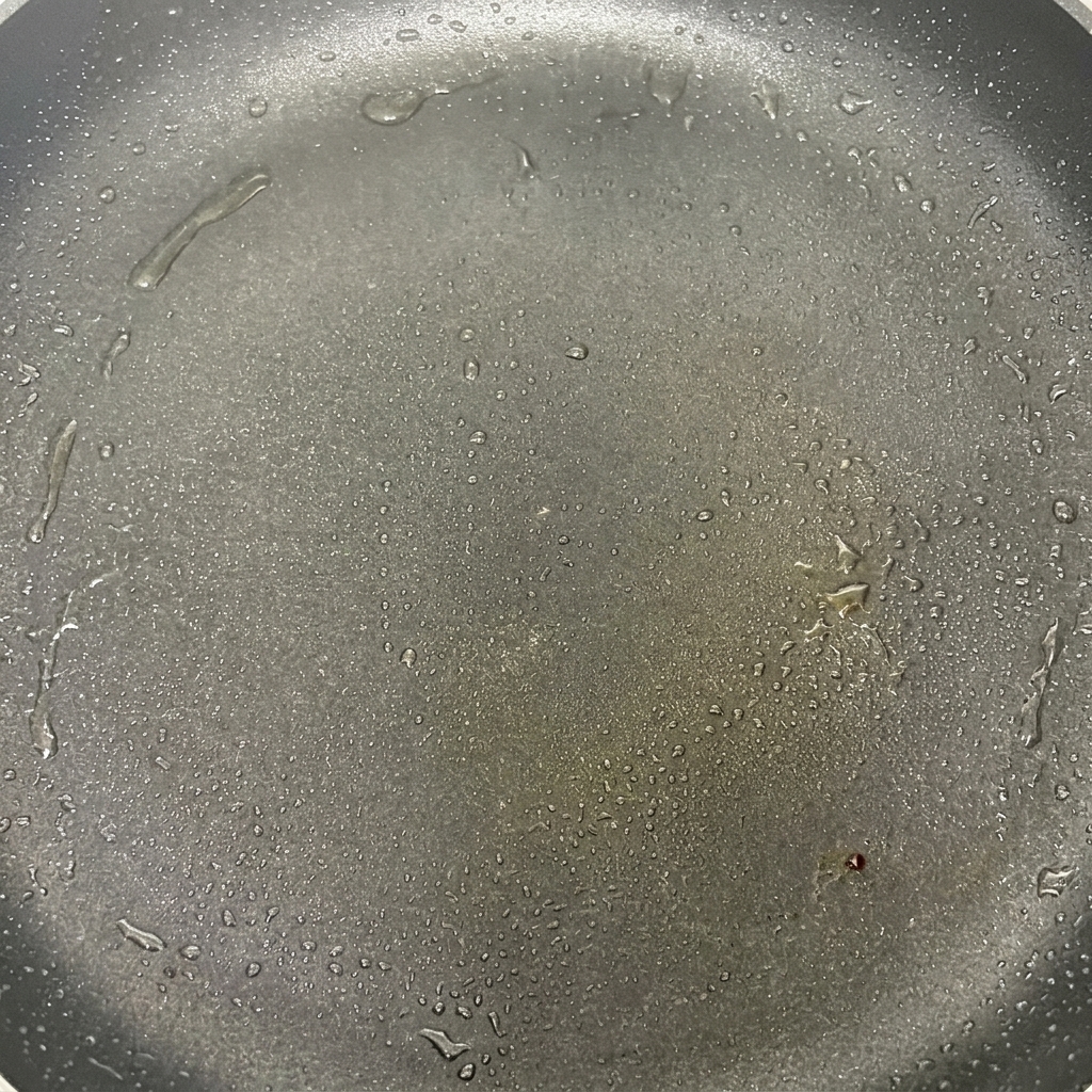 熱したフライパンで油とともに焼かれ、少し焼き色がつき始めたマッシュルームの傘。