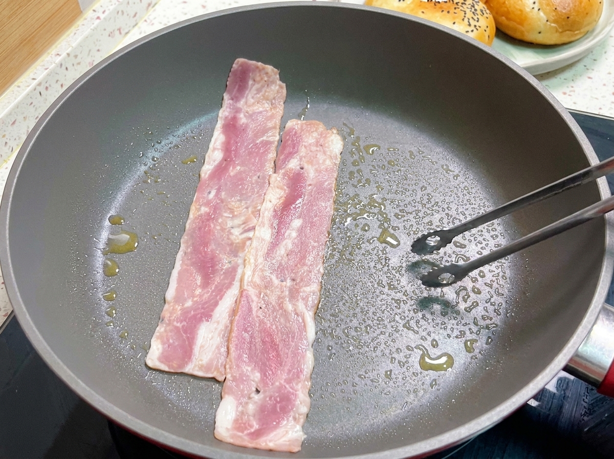 熱いフライパンでベーコンを焼き、トングでひっくり返している様子。
