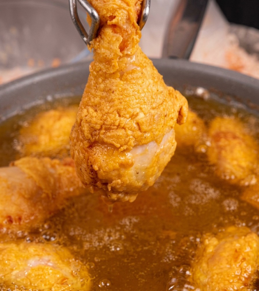 トングでチキンを持ち上げ、鍋の上で油を切っている様子。