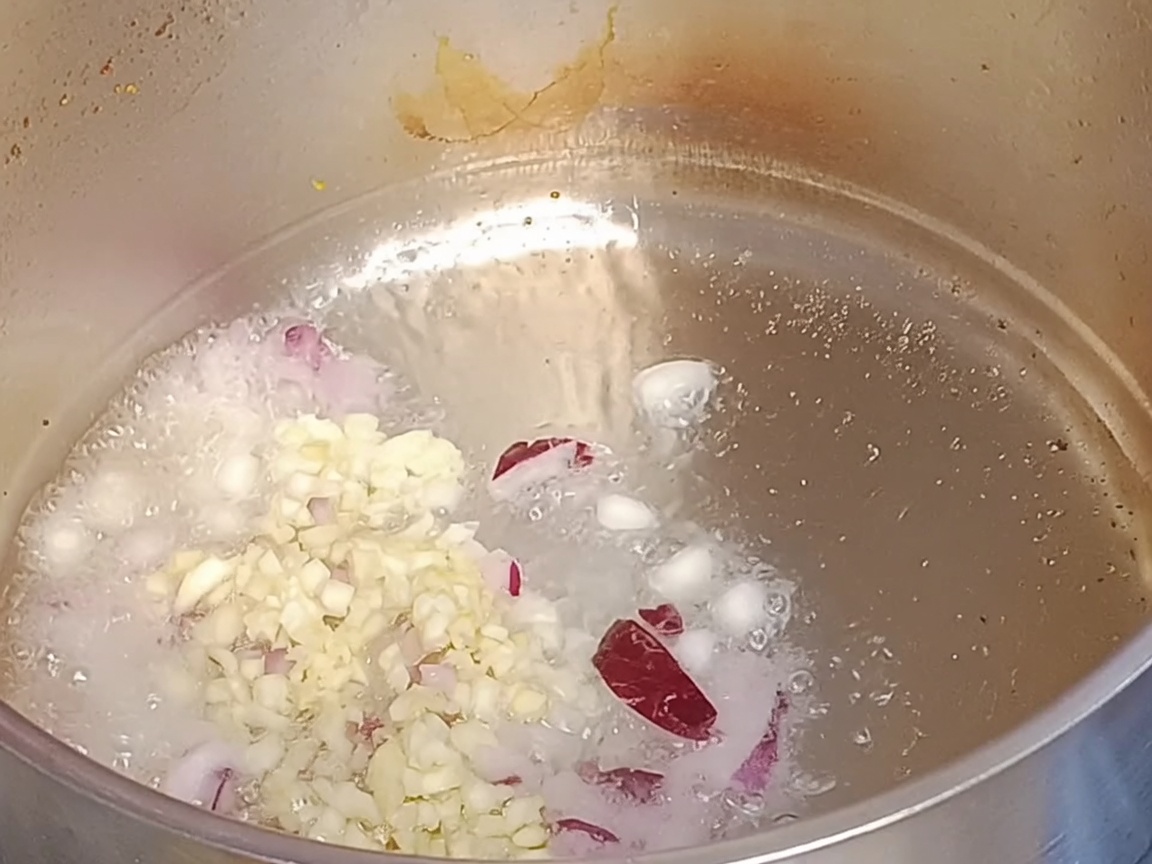 鍋で熱した油でみじん切りの赤玉ねぎとにんにくを炒めている様子。
