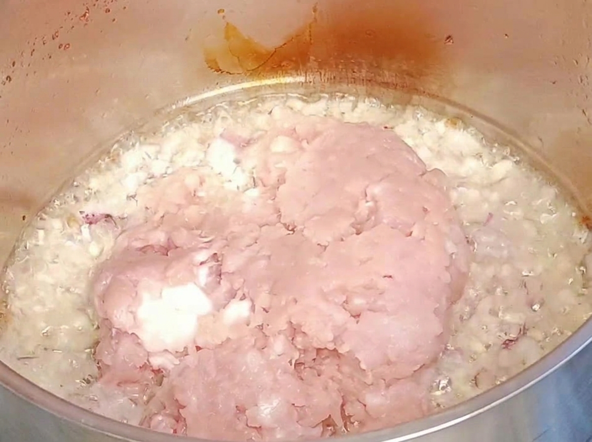 炒めた玉ねぎとにんにくの入った鍋に生のひき肉を加えている様子。