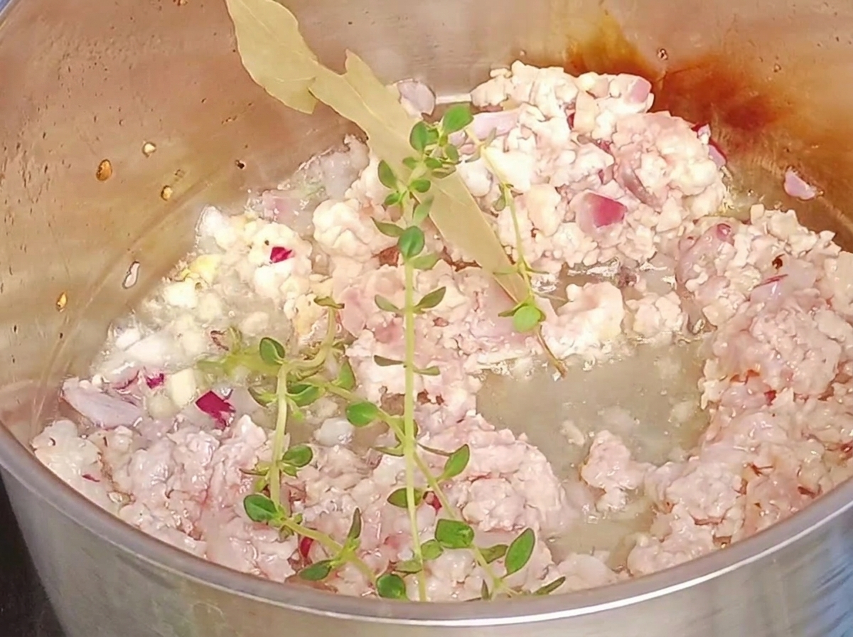 鍋の中のひき肉に生のタイムとローリエを加えている様子。
