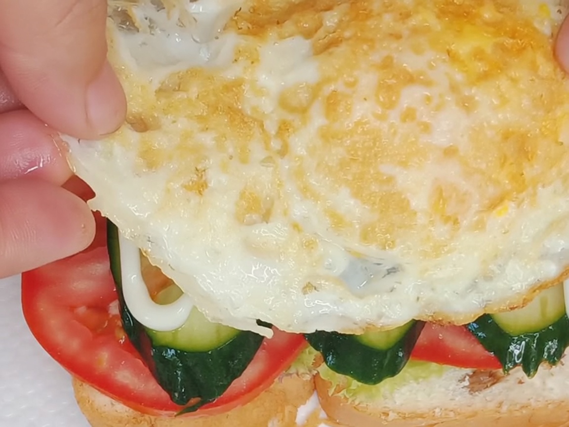 綺麗に焼けた目玉焼きをサンドイッチの一番上にのせている様子。