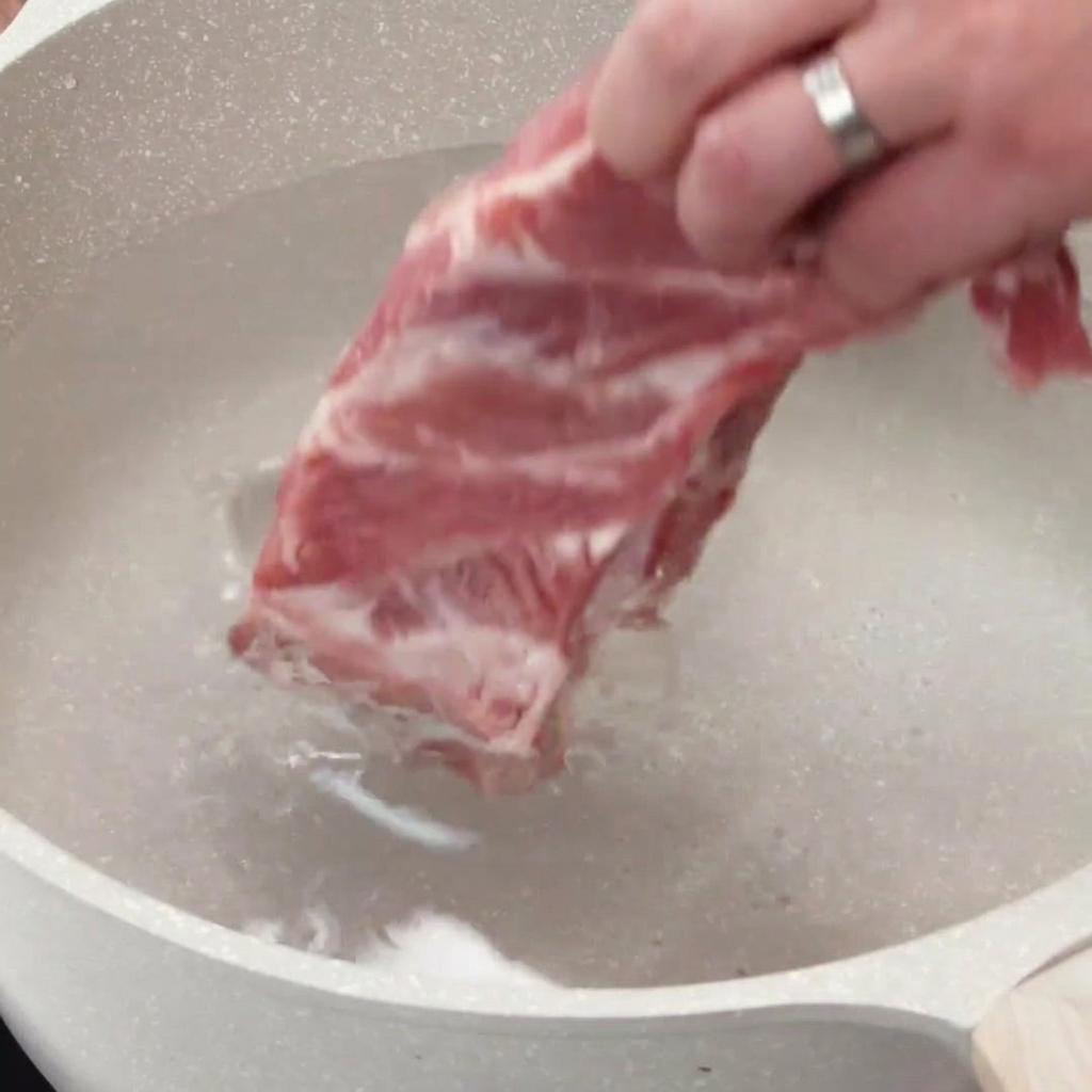 生のポークリブを冷水の入った大きな鍋に入れている様子