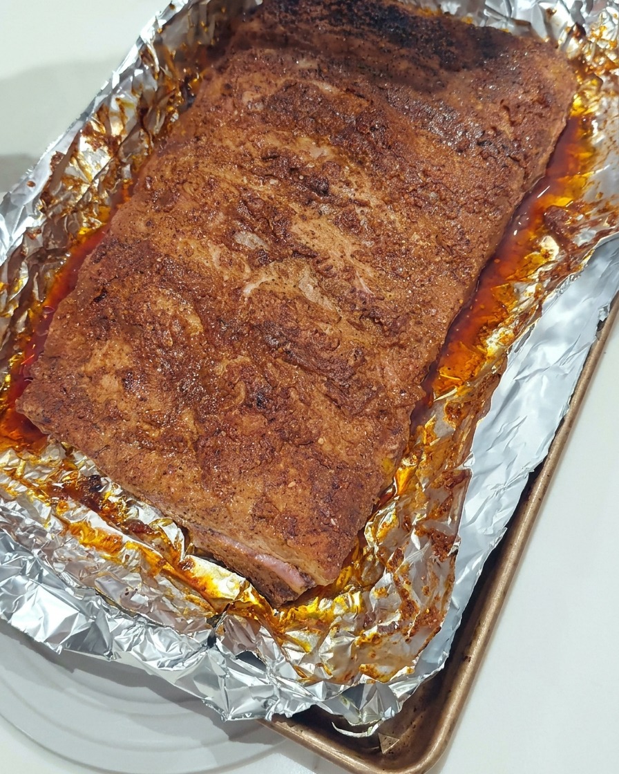 ホイルを敷いた天板の上で、ローストしたポークリブにシリコンブラシで濃厚なBBQソースを塗っている様子。