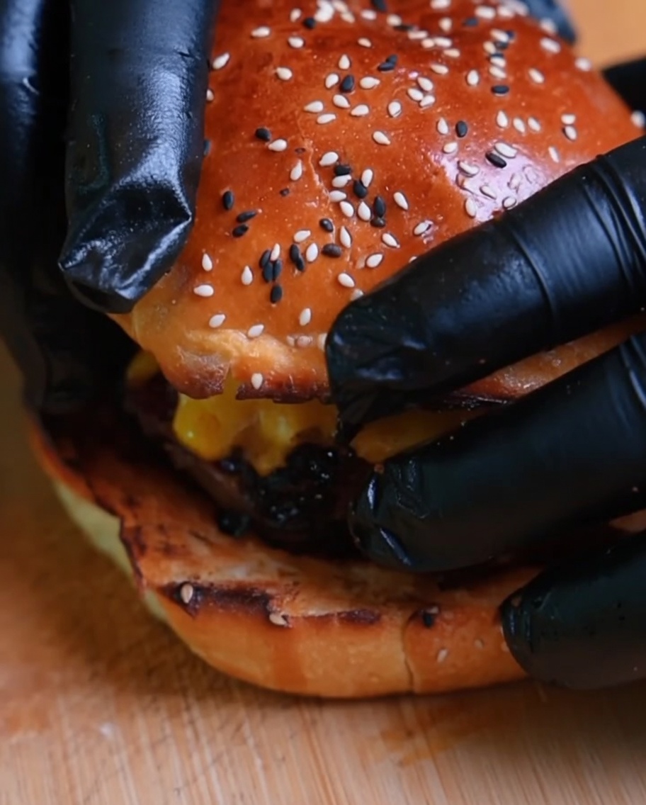手袋をした手で仕上げたバーガーの上に上のバンズをのせている様子。