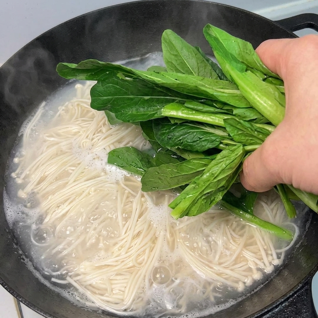 茹でている麺の鍋に新鮮な青菜を加える様子。