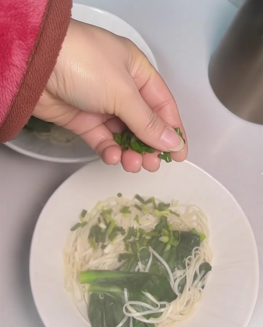 麺の上に刻んだねぎを振りかけている手元。