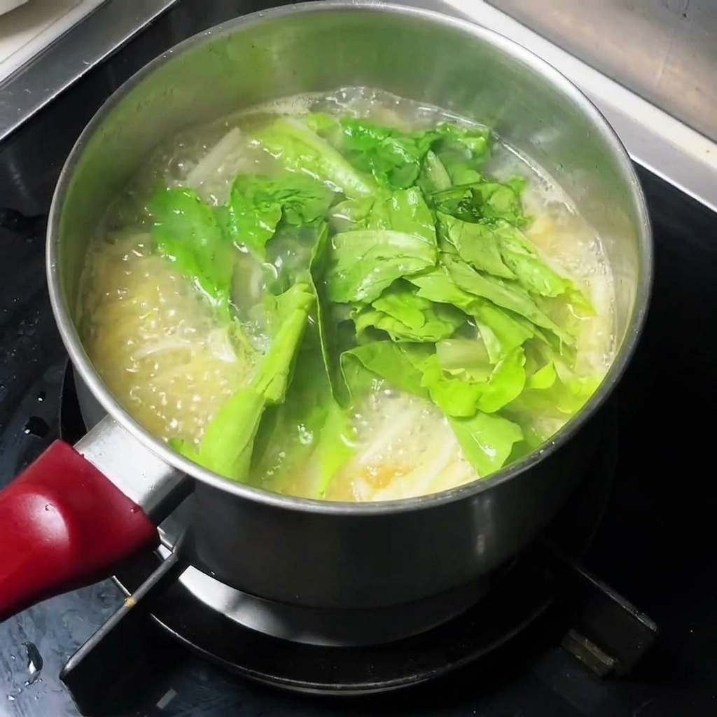 沸騰するスープに新鮮な葉物野菜が加えられている様子。
