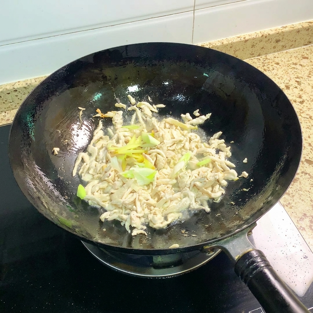 炒めた鶏肉に刻みねぎと生姜を加えて炒めている様子。