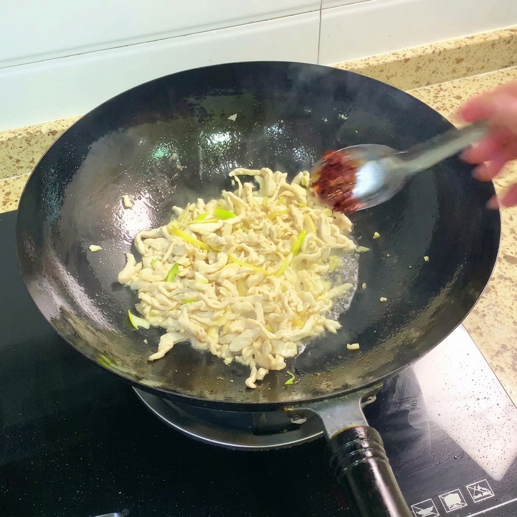 鶏肉の混合物にピーシェン豆板醤を加えて炒めている様子。