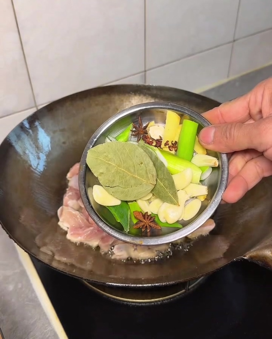 さまざまなスパイスを鶏肉の入った鍋に加える様子。
