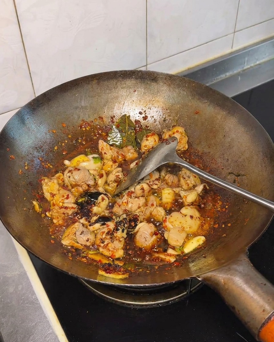 醤油などの調味料を炒めた鶏肉に加える様子。