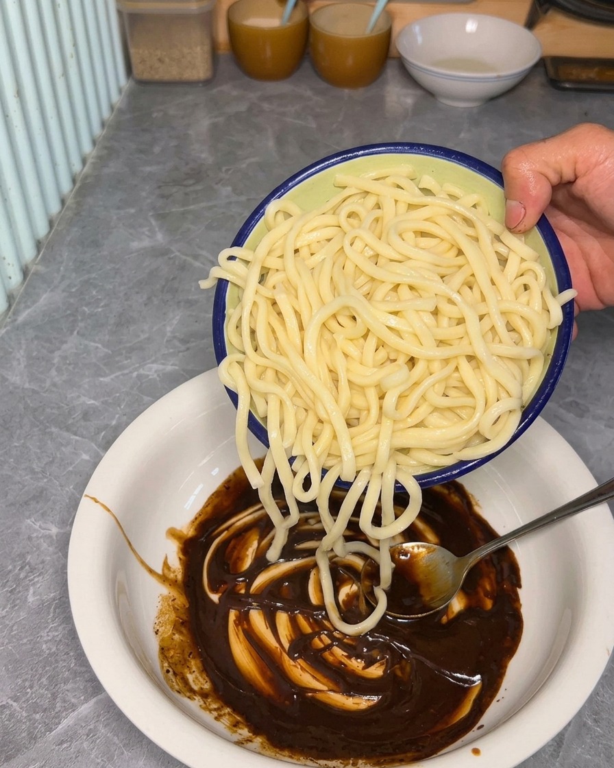 茹で上がった麺をソースの入った器に入れる様子。