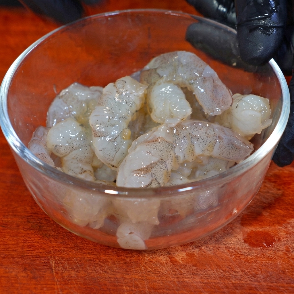 ガラスボウルの中で調味料と片栗粉をまぶしてマリネするエビ。