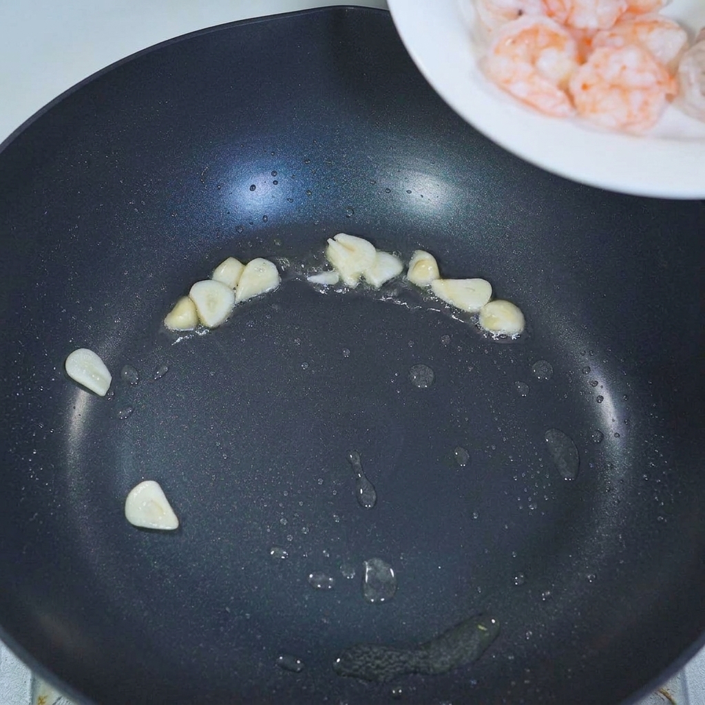 炒めたニンニクの入ったフライパンに茹でたエビを加えている様子。