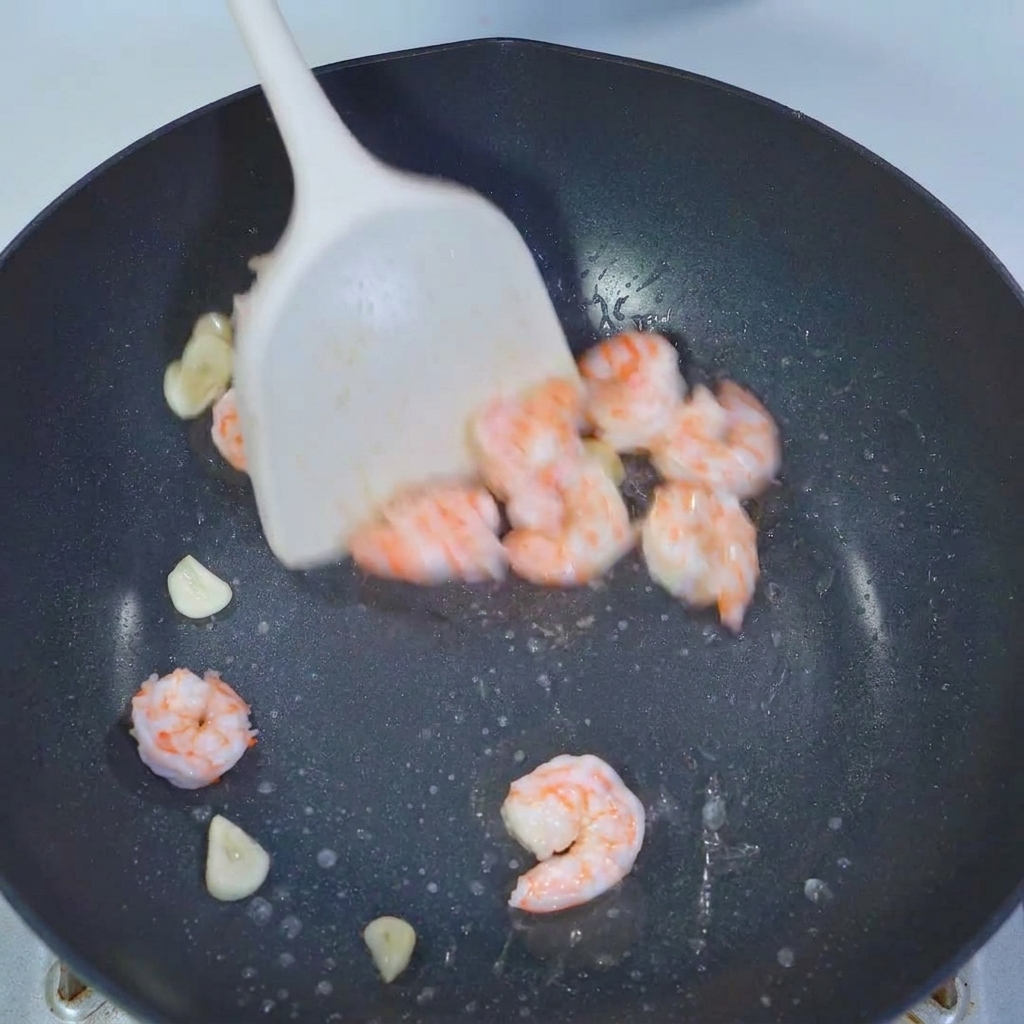白いスパチュラでオクラとエビをフライパンの中で炒め合わせている様子。