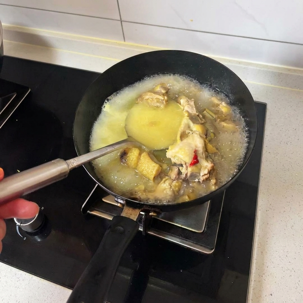 黒い中華鍋の中で熱々のチキンブロスと調理済みの鶏肉をレードルで混ぜている様子。