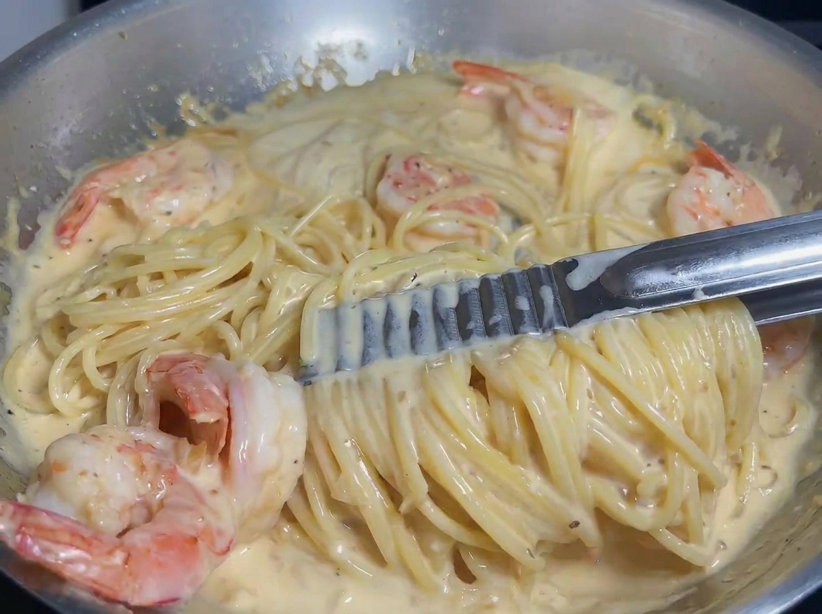 トングを使ってパスタとエビをクリームソースにしっかりと絡めている様子。