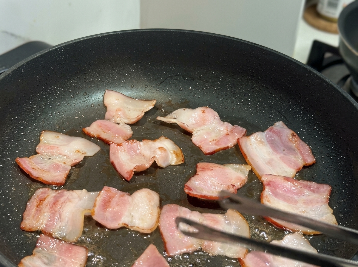 テフロン加工のフライパンでベーコンが炒められている様子。
