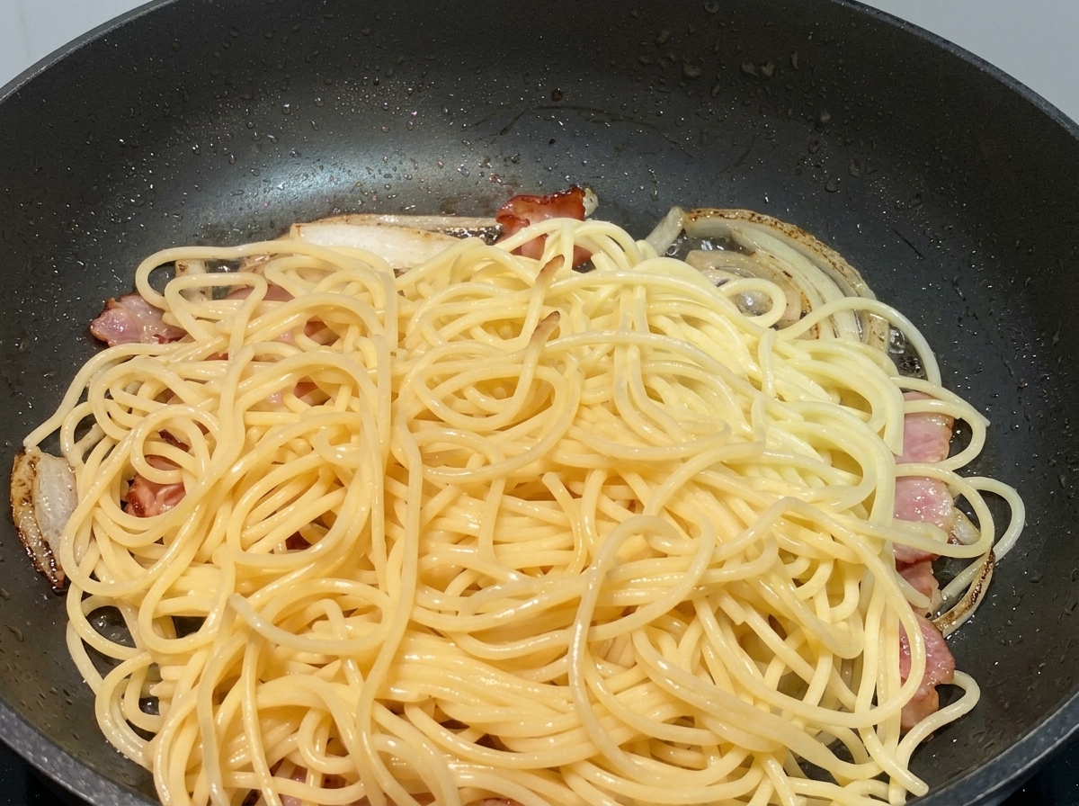 炒めた玉ねぎとベーコンが入ったフライパンに、パスタが投入される直前の様子。