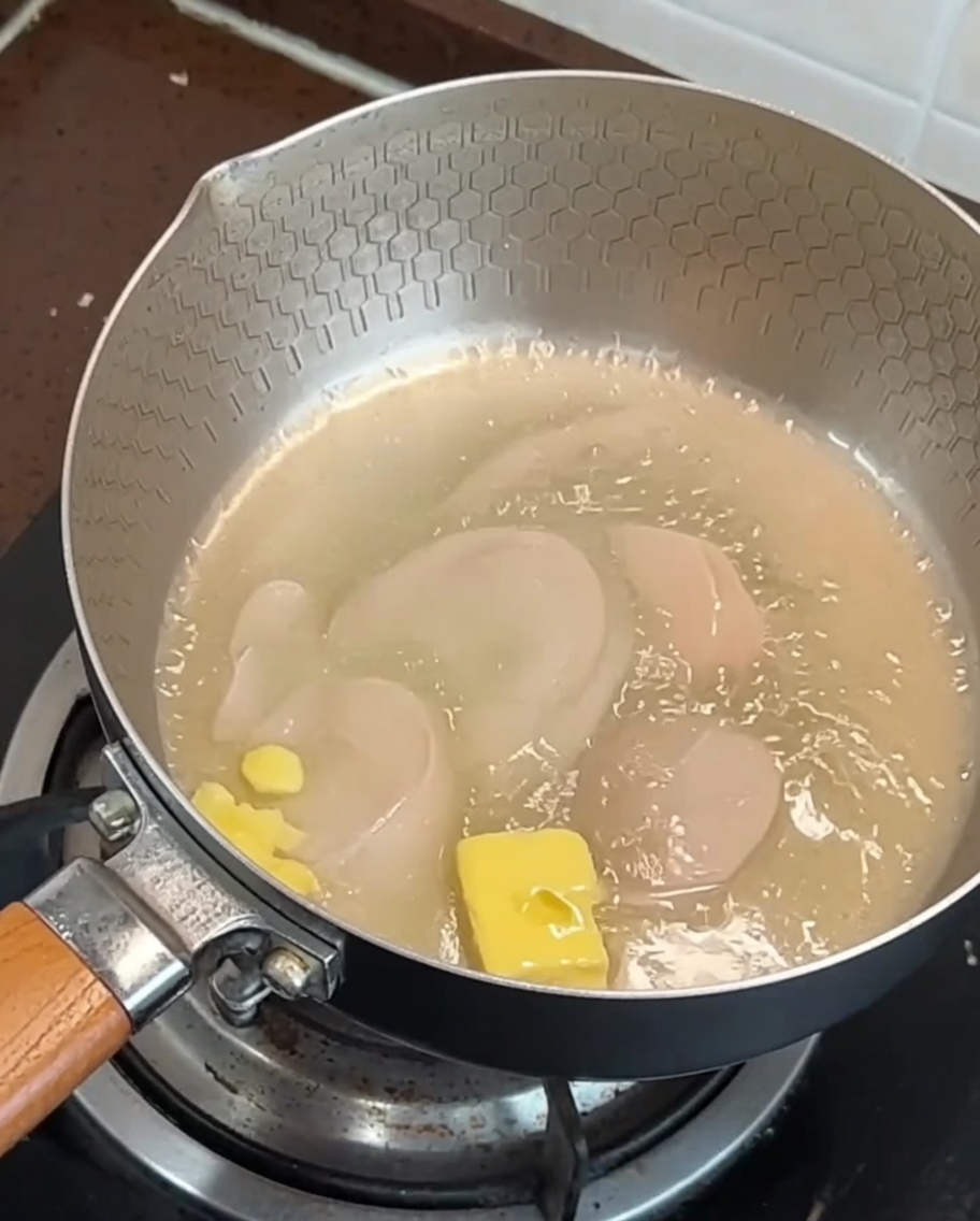 溶けたバターが入ったフライパンで焼かれているベーコンのスライスとにんにく。