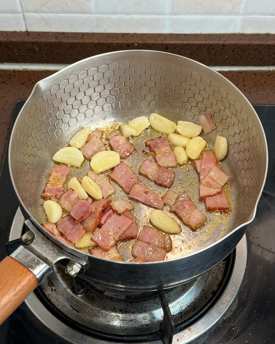 スライスされたマッシュルーム、ベーコン、にんにくが一緒にフライパンで炒められている様子。