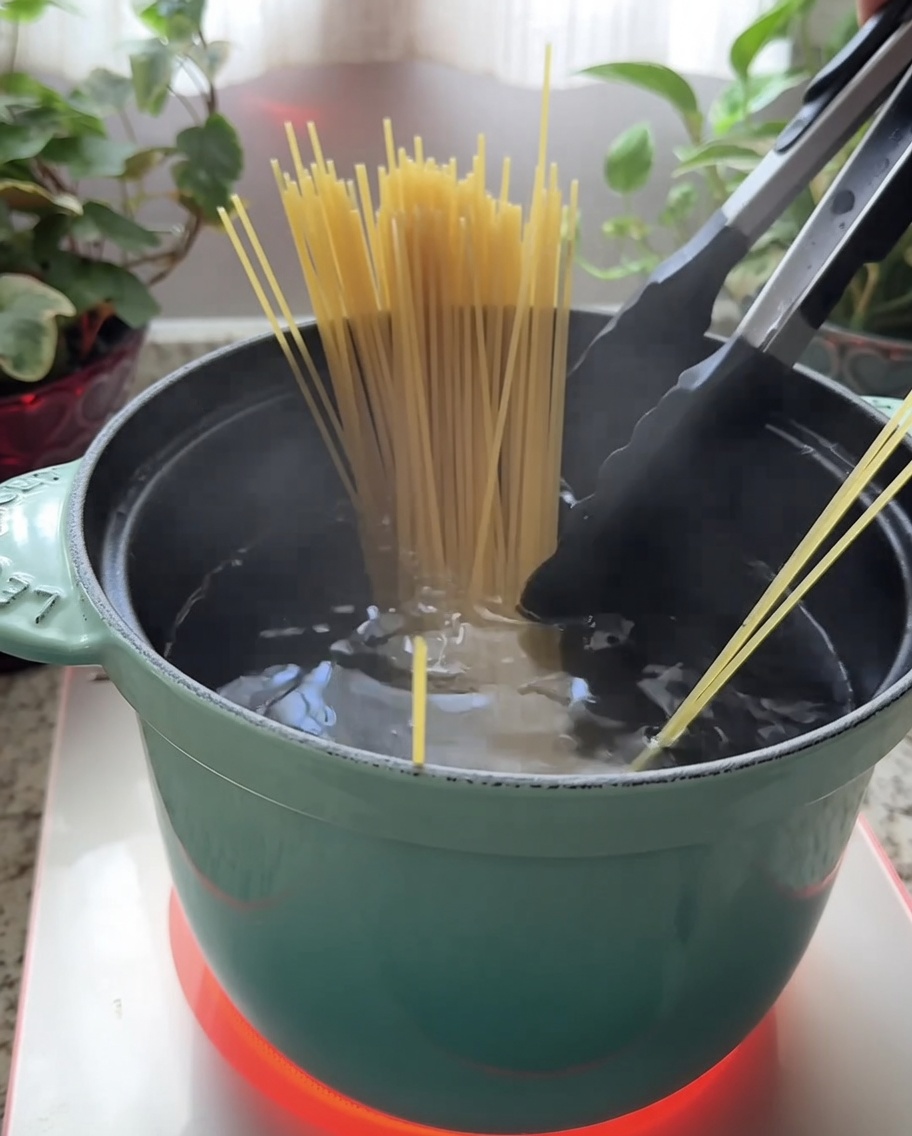 沸騰したお湯が入った緑色の鍋に、乾燥スパゲッティを入れているところ。