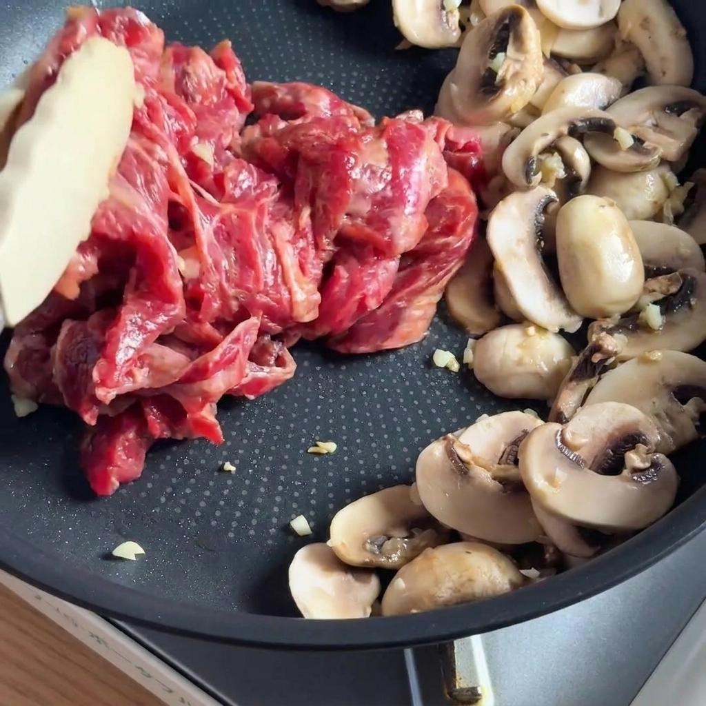 フライパンできのこと一緒に炒められる下味をつけた牛肉。