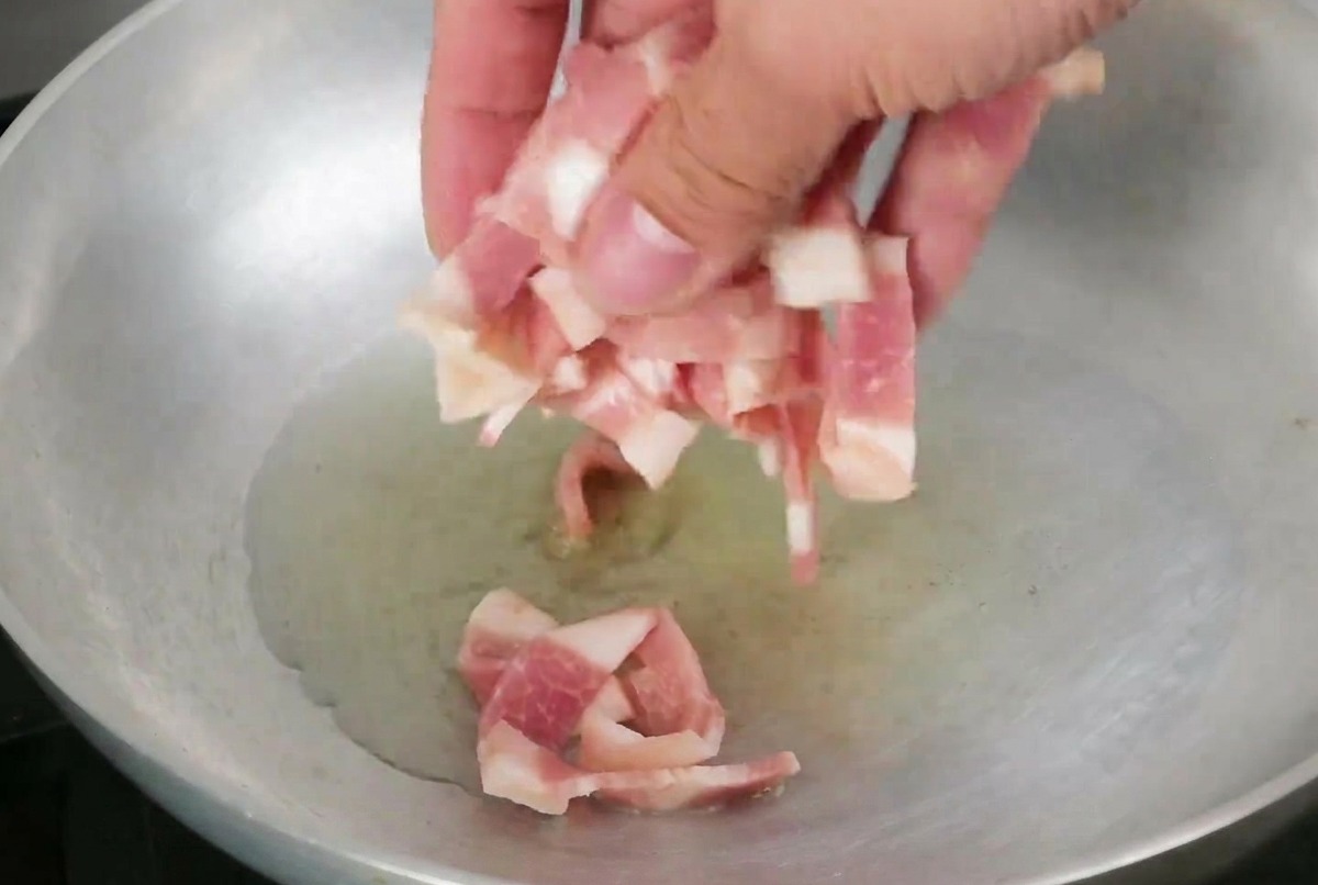 オリーブオイルの中で焼かれているベーコンの細切り。