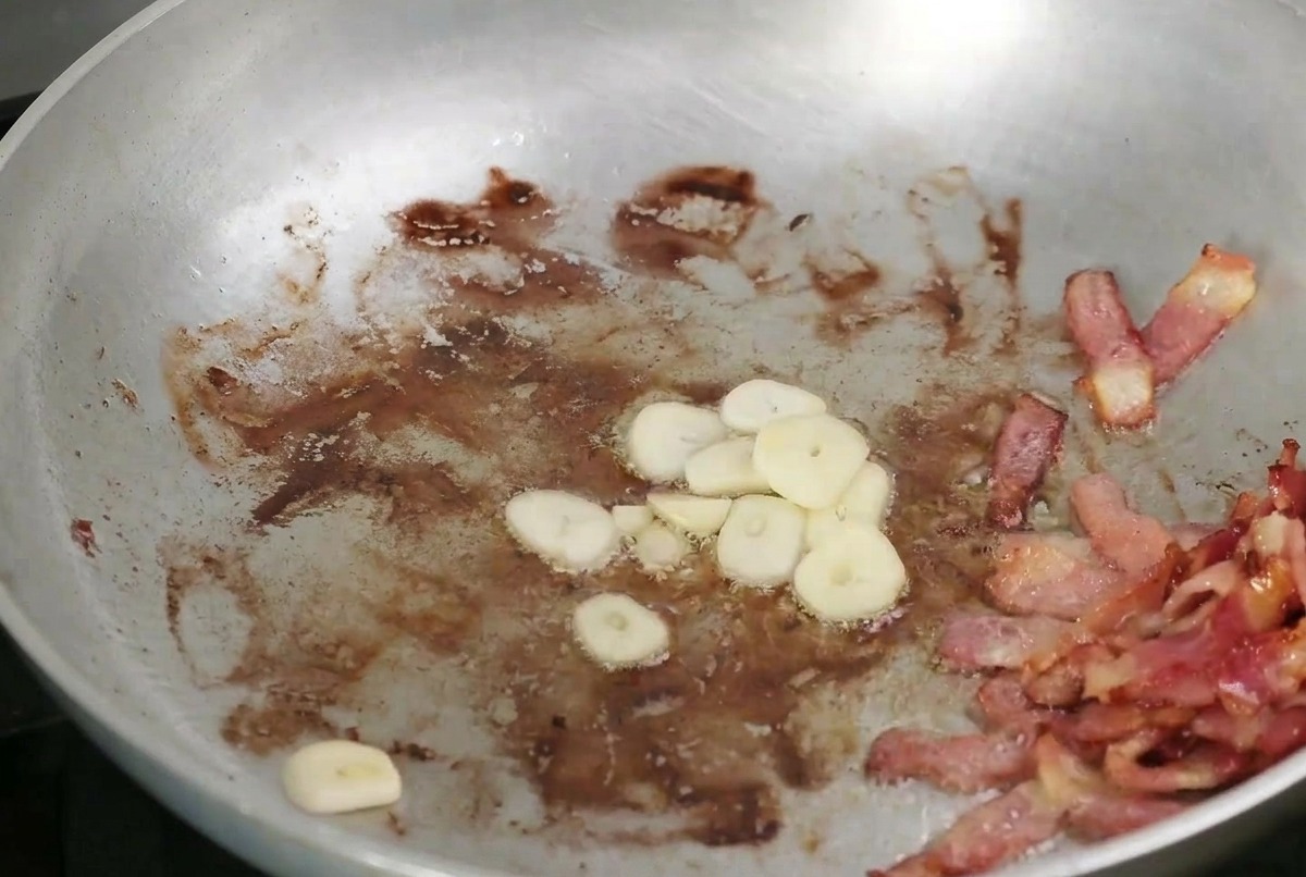 カリカリのベーコンと一緒にフライパンで焼かれている、スライスしたニンニクとキノコ。