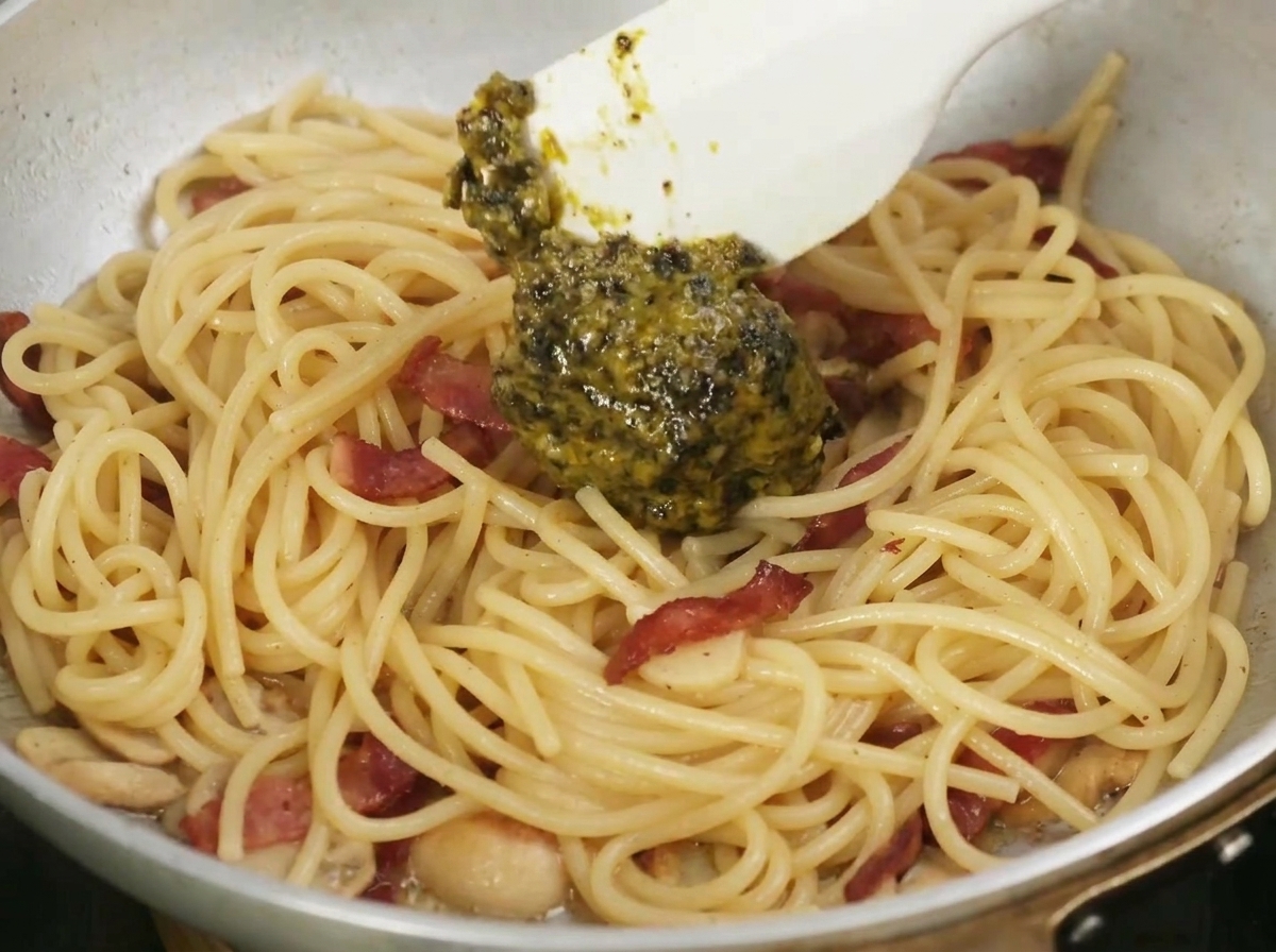 スパチュラで黒い芳醇な黒トリュフソースを、調理中のパスタに混ぜ合わせている様子。