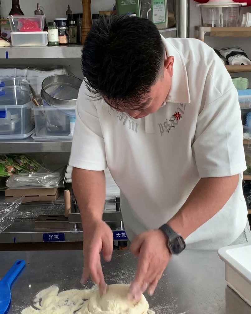 平らで丸いピザのベースを作るために、生地のボールを上から押さえている両手。