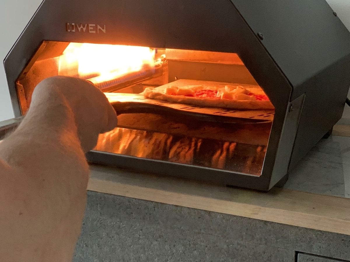 ピザピールを使って、焼く前のマルゲリータピザを高温の卓上ガスピザオーブンに入れている様子。