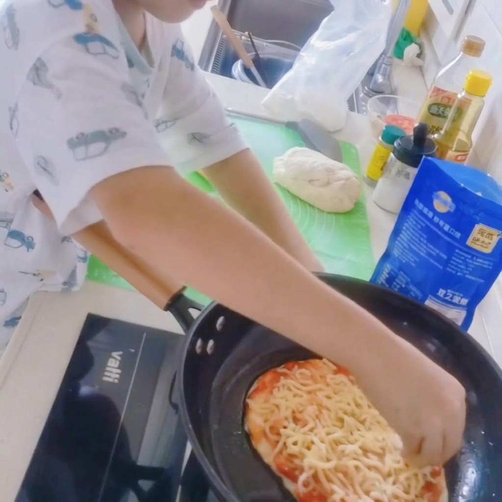 フライパンの中のピザベースに、たっぷりのシュレッドモッツァレラチーズを乗せている様子。